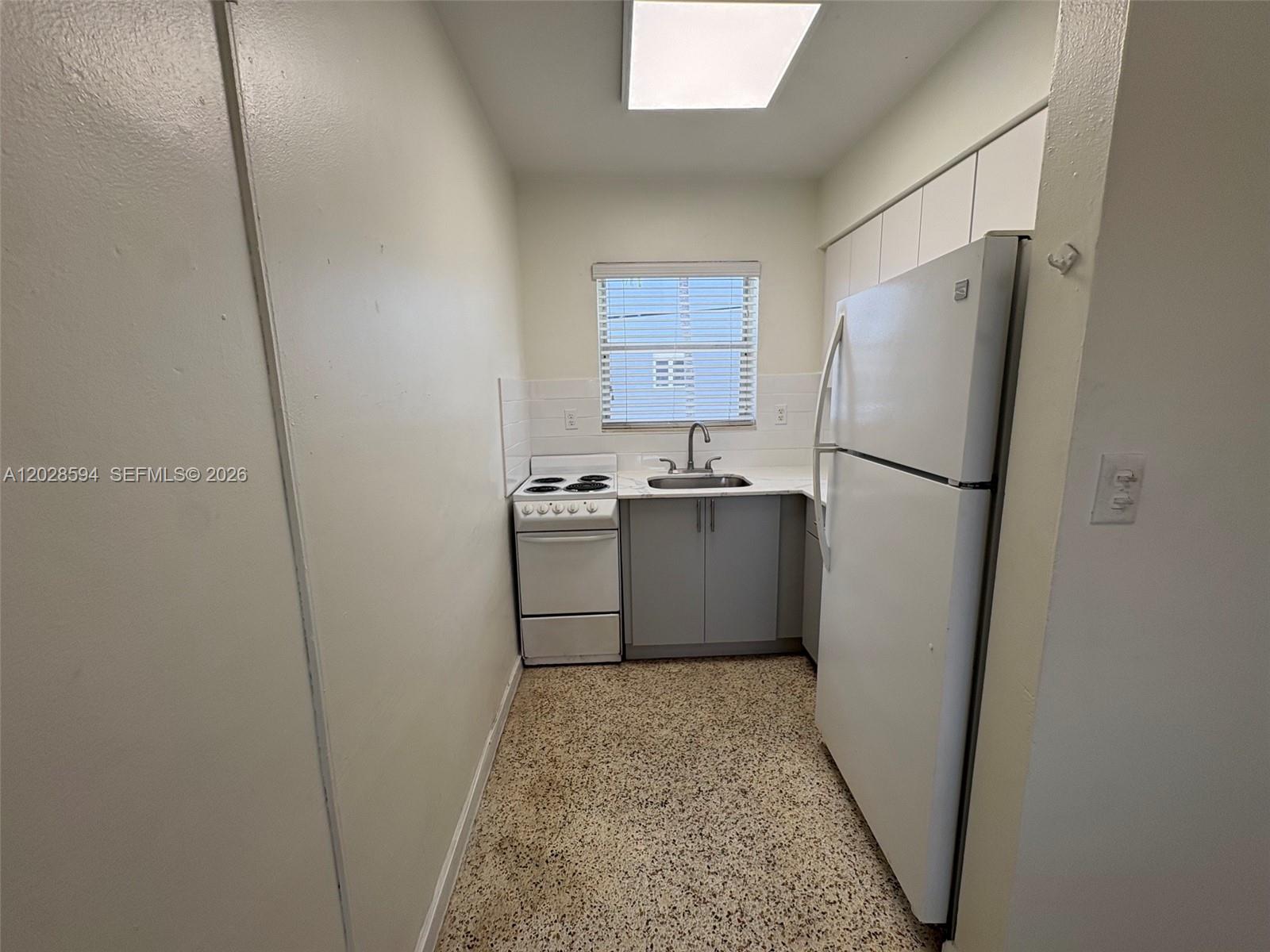 A small galley kitchen features white appliances, gray cabinets, and a speckled floor — 320 W 10th St # 3, Hialeah FL 33010, HIALEAH, FL
