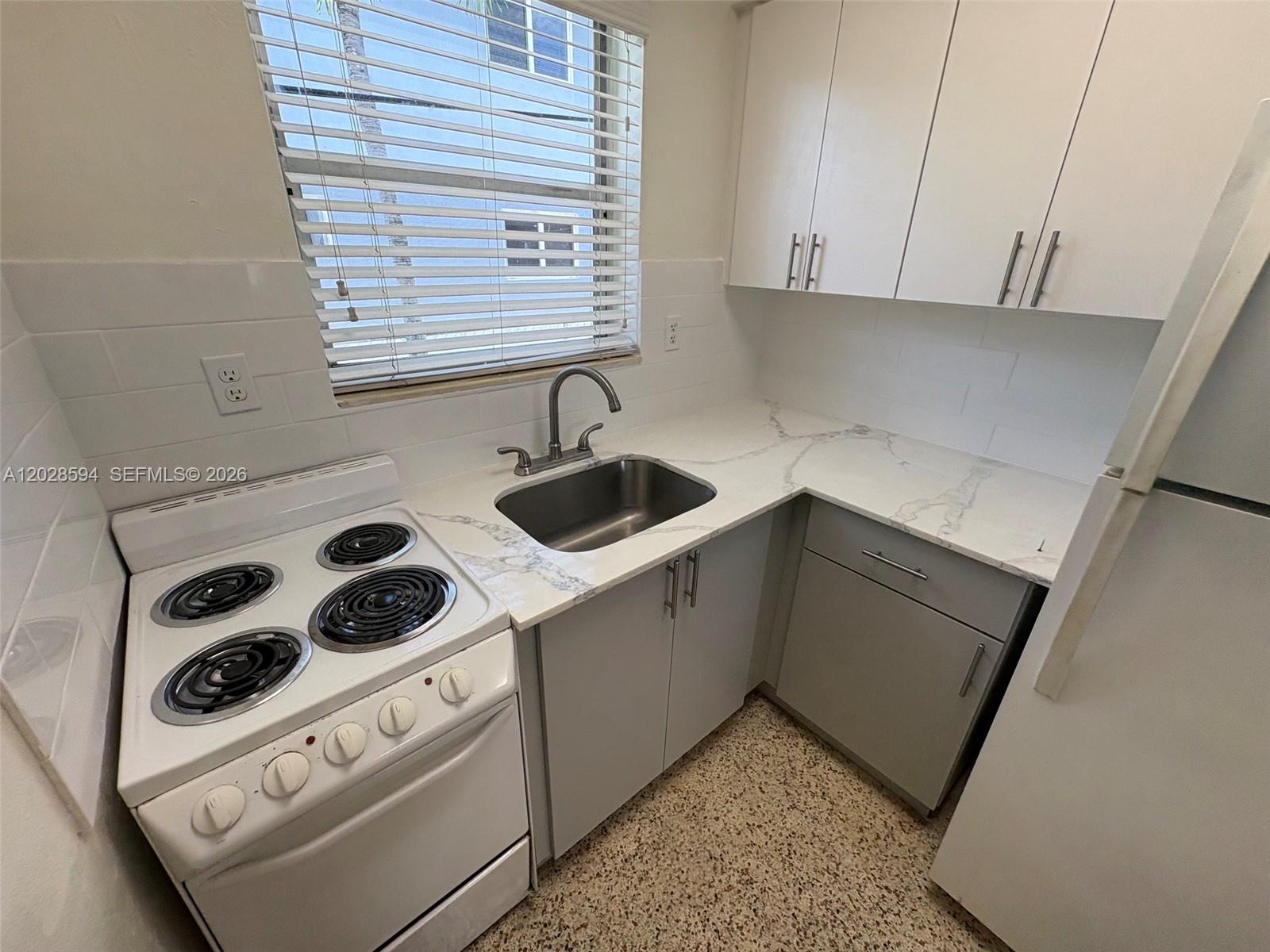 A small kitchen features white cabinets, gray lower cabinets, marble-look countertops, and a white stove — 320 W 10th St # 3, Hialeah FL 33010, HIALEAH, FL