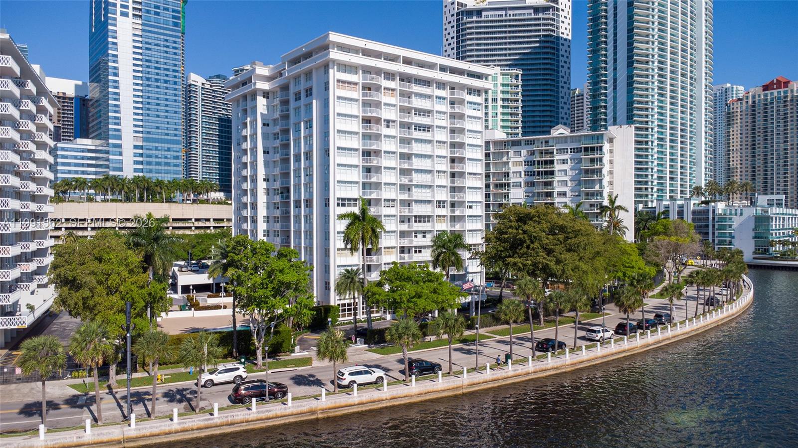 An aerial view shows a white multi-story residential building situated along a waterfront road — 1420 Brickell Bay Dr # 1003A, Miami FL 33131, MIAMI, FL