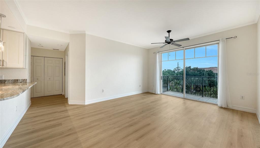 An empty living room with light wood flooring, a ceiling fan, and a balcony entrance — 1064 N TAMIAMI TRAIL UNIT 1435, SARASOTA, FL
