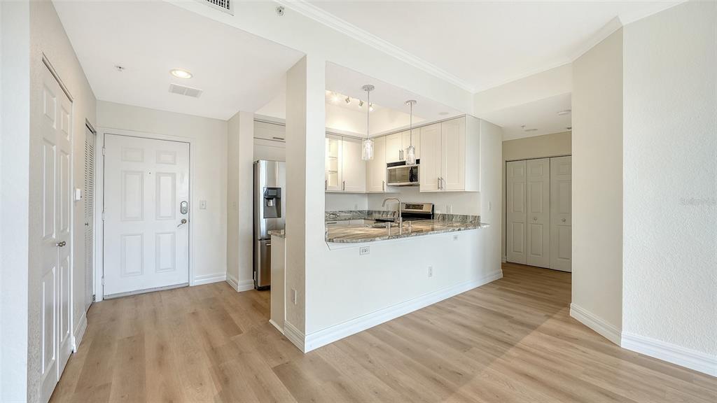 A kitchen with white cabinets and stone countertops opens into a living area with wood flooring — 1064 N TAMIAMI TRAIL UNIT 1435, SARASOTA, FL