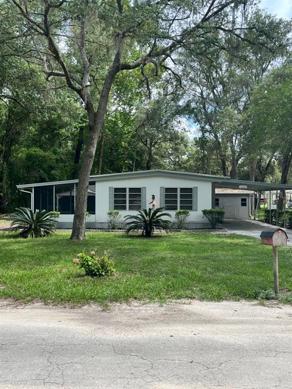 A single-story manufactured home with a screened porch, carport, and mature trees in the yard — 11012 NW 113TH PLACE, CHIEFLAND, FL