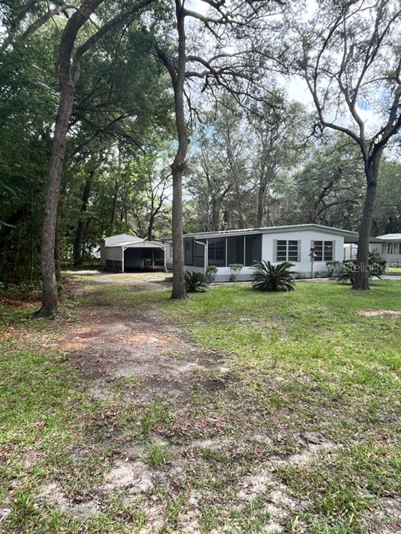 A white mobile home with a screened porch and a detached carport sits among trees — 11012 NW 113TH PLACE, CHIEFLAND, FL