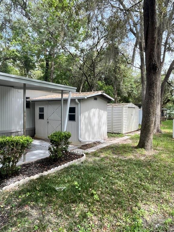 Two storage sheds sit on a grassy lot next to a mobile home with a carport — 11012 NW 113TH PLACE, CHIEFLAND, FL