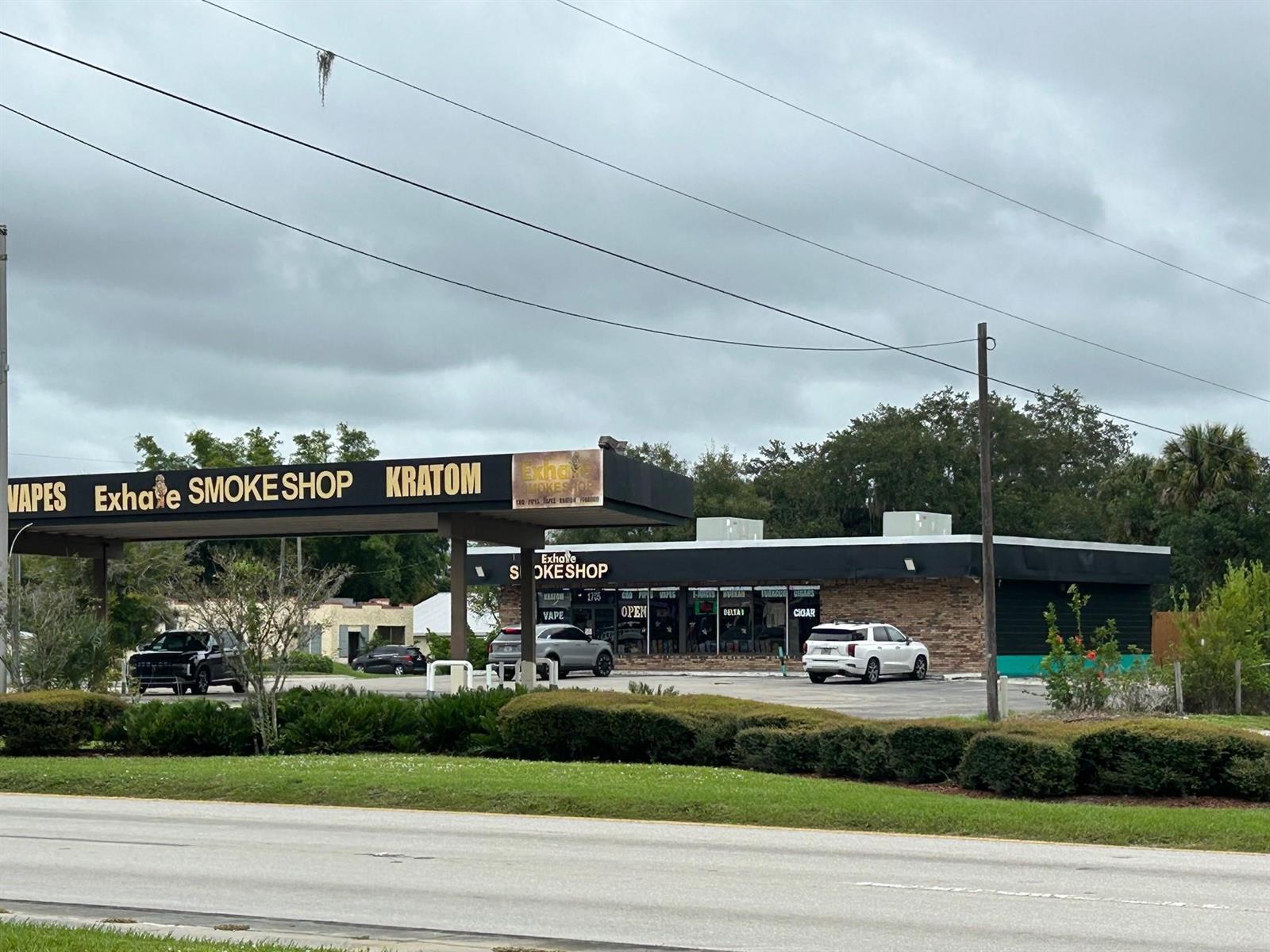 A commercial smoke shop building with a large parking lot under a cloudy sky — 1705 S Parrott Avenue, Okeechobee FL 34974, OKEECHOBEE, FL