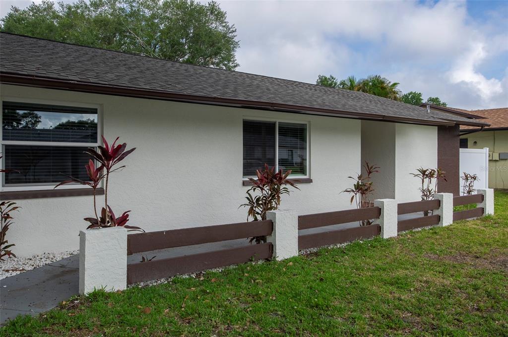 A single-story house exterior features white stucco walls, brown trim, and a low wooden fence — 1689 MONTEREY DRIVE, CLEARWATER, FL