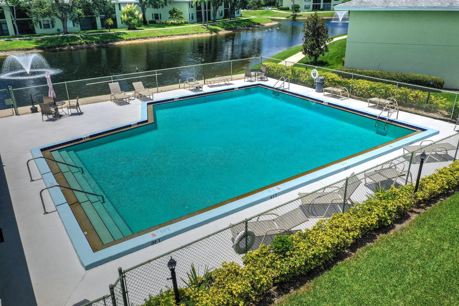 An outdoor rectangular swimming pool is enclosed by a chain-link fence near a pond — 601 Sabal Ridge Circle # A, Palm Beach Gardens FL 33418, PALM BEACH GARDENS, FL
