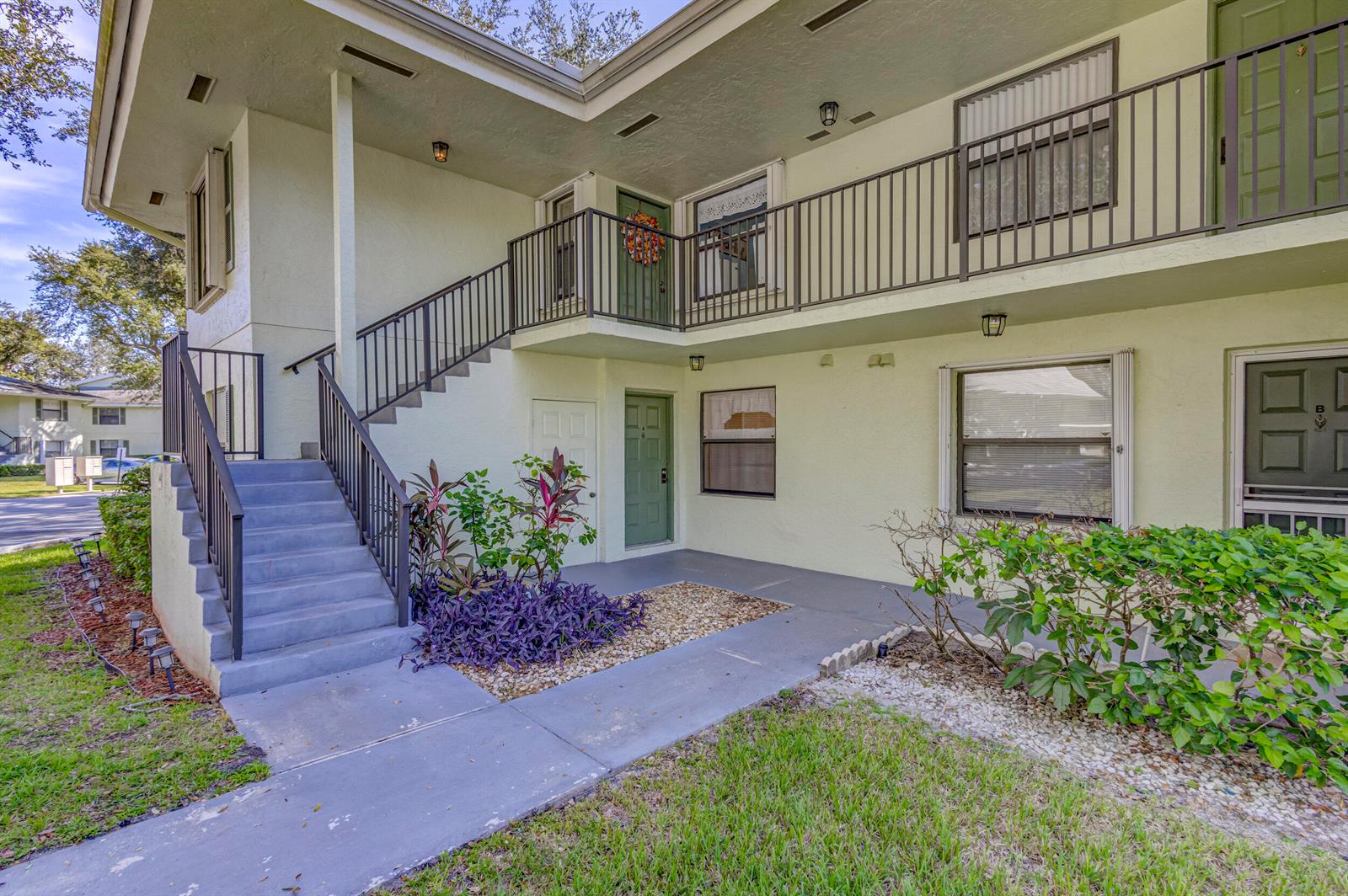 An exterior view of a two-story apartment building with stairs leading to an upper balcony — 601 Sabal Ridge Circle # A, Palm Beach Gardens FL 33418, PALM BEACH GARDENS, FL
