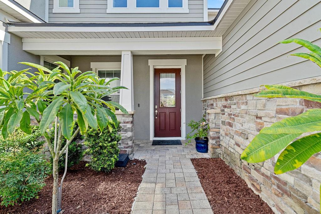 A paved walkway leads to a front entrance with a red door and stone siding — 14897 ELLINGSWORTH LANE, WINTER GARDEN, FL