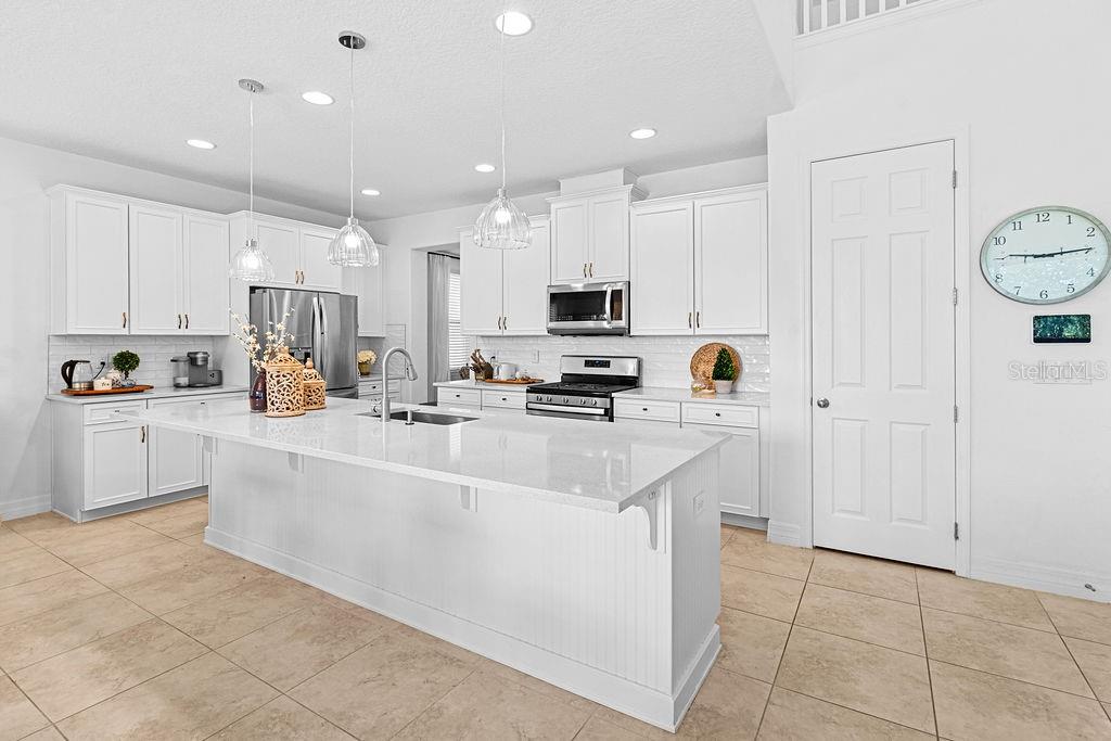 A bright foyer features a staircase with a wooden railing and tile flooring — 14897 ELLINGSWORTH LANE, WINTER GARDEN, FL