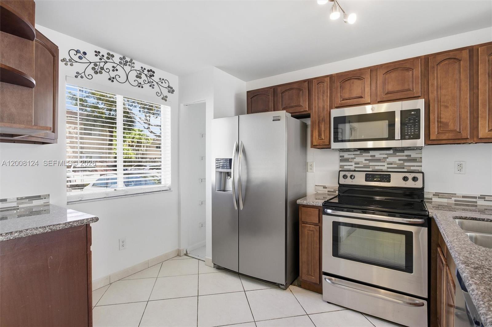 A kitchen features wooden cabinets, stainless steel appliances, granite countertops, and white tile flooring — 17530 SW 139th Ct, Miami FL 33177, MIAMI, FL