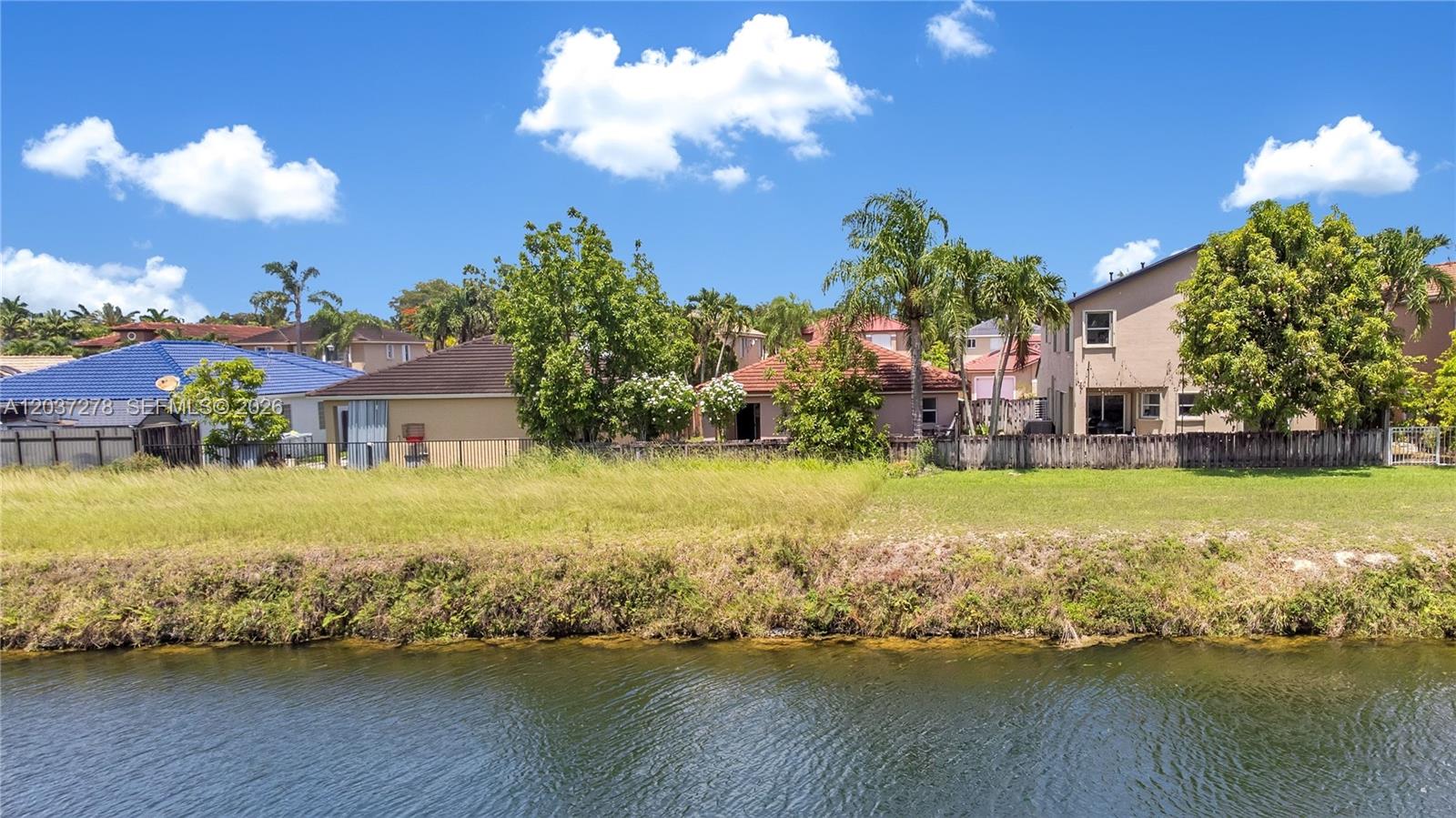 A view of a grassy backyard bordering a canal with several houses in the background — 14530 SW 156th Ave, Miami FL 33196, MIAMI, FL