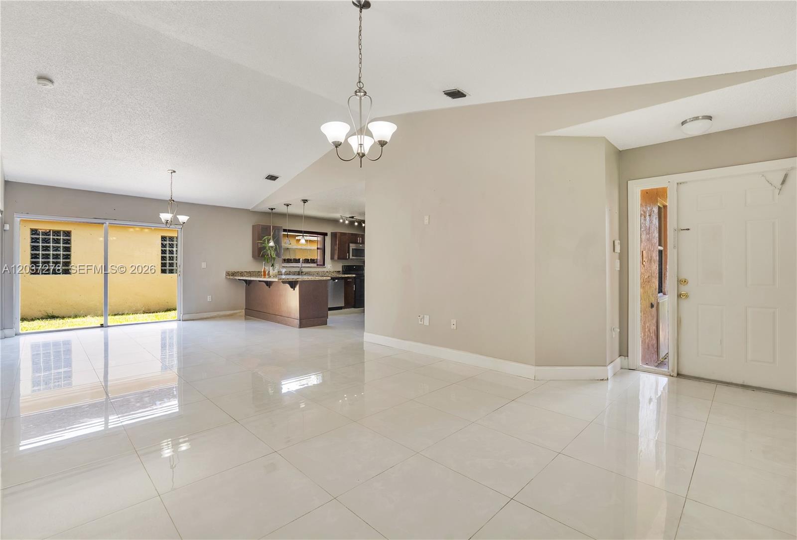 This open-concept living area features white tile flooring, a kitchen island, and sliding glass doors — 14530 SW 156th Ave, Miami FL 33196, MIAMI, FL