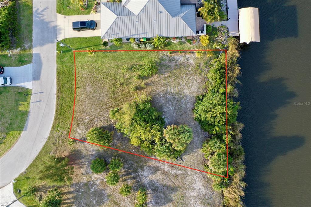 An aerial view shows a vacant, trapezoidal waterfront lot outlined in red next to a house — 14702 LILLIAN CIRCLE, PORT CHARLOTTE, FL