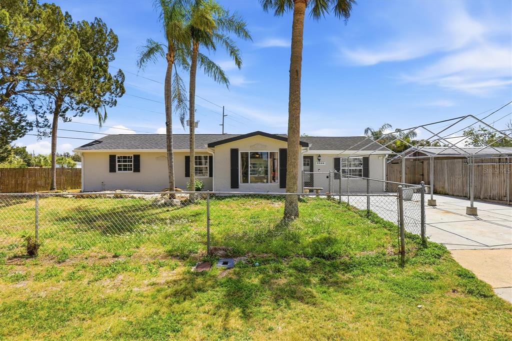 A single-story house with a chain-link fence, palm trees, and a metal carport structure — 7114 FAIR LANE, HUDSON, FL