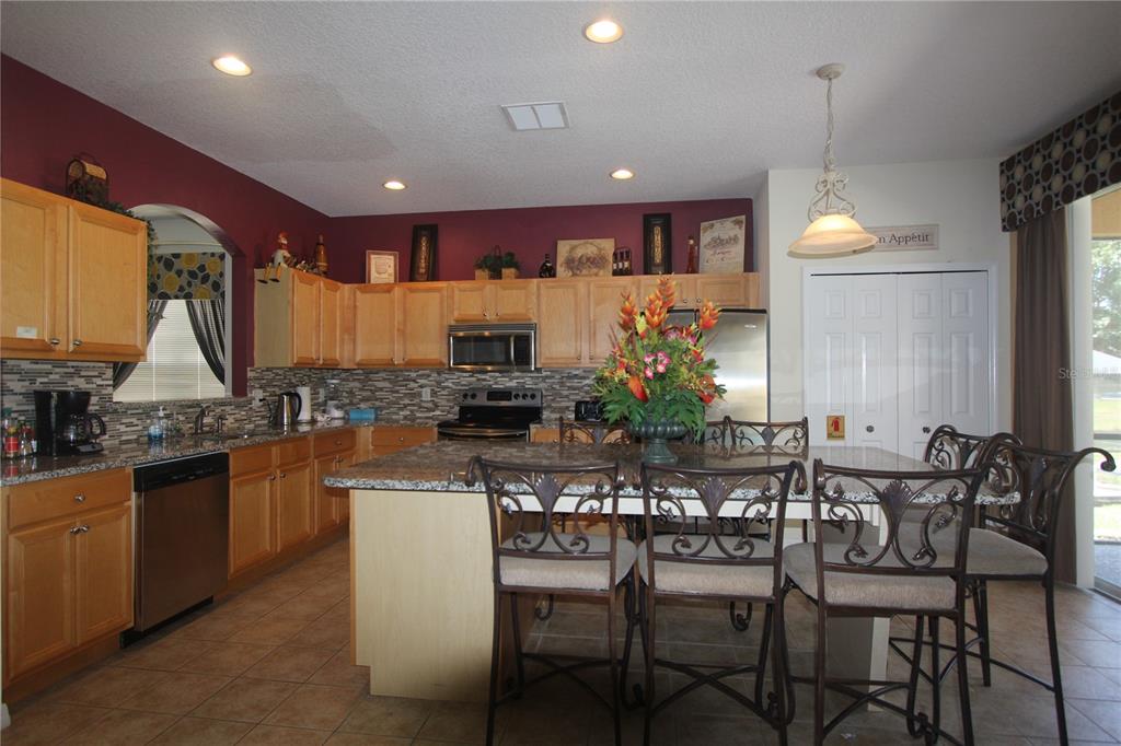 A kitchen with light wood cabinets, granite countertops, a center island, and dark red walls — 8475 OASIS KEY COVE, KISSIMMEE, FL