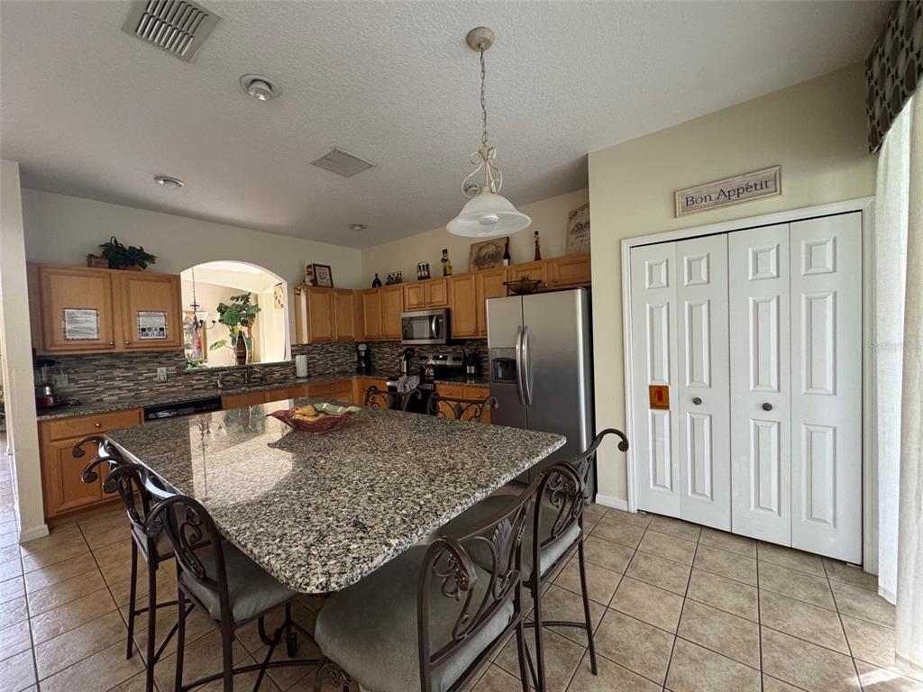 A kitchen features light wood cabinets, granite countertops, a large island, and stainless steel appliances — 8475 OASIS KEY COVE, KISSIMMEE, FL