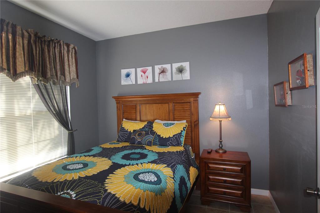 A bedroom features a wooden bed frame, floral bedding, a nightstand with a lamp, and gray walls — 8475 OASIS KEY COVE, KISSIMMEE, FL