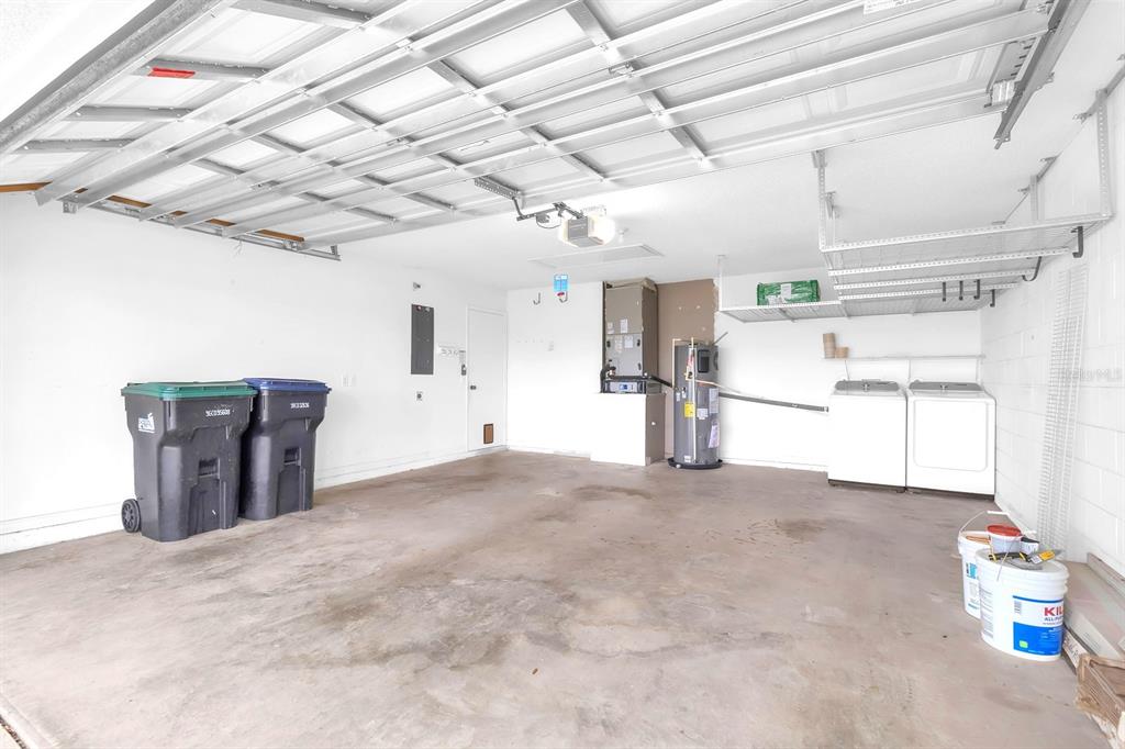 A garage with a concrete floor, two trash bins, a washer, dryer, and water heater — 8141 FORT THOMAS WAY, ORLANDO, FL