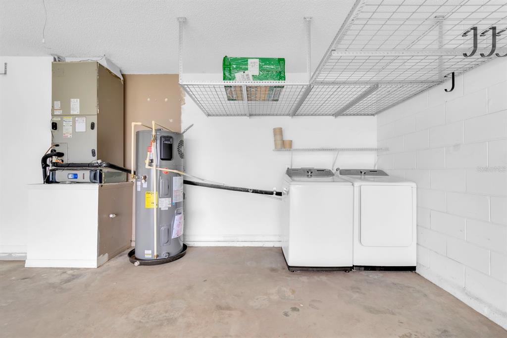 A garage space containing a water heater, HVAC unit, laundry appliances, and overhead storage racks — 8141 FORT THOMAS WAY, ORLANDO, FL