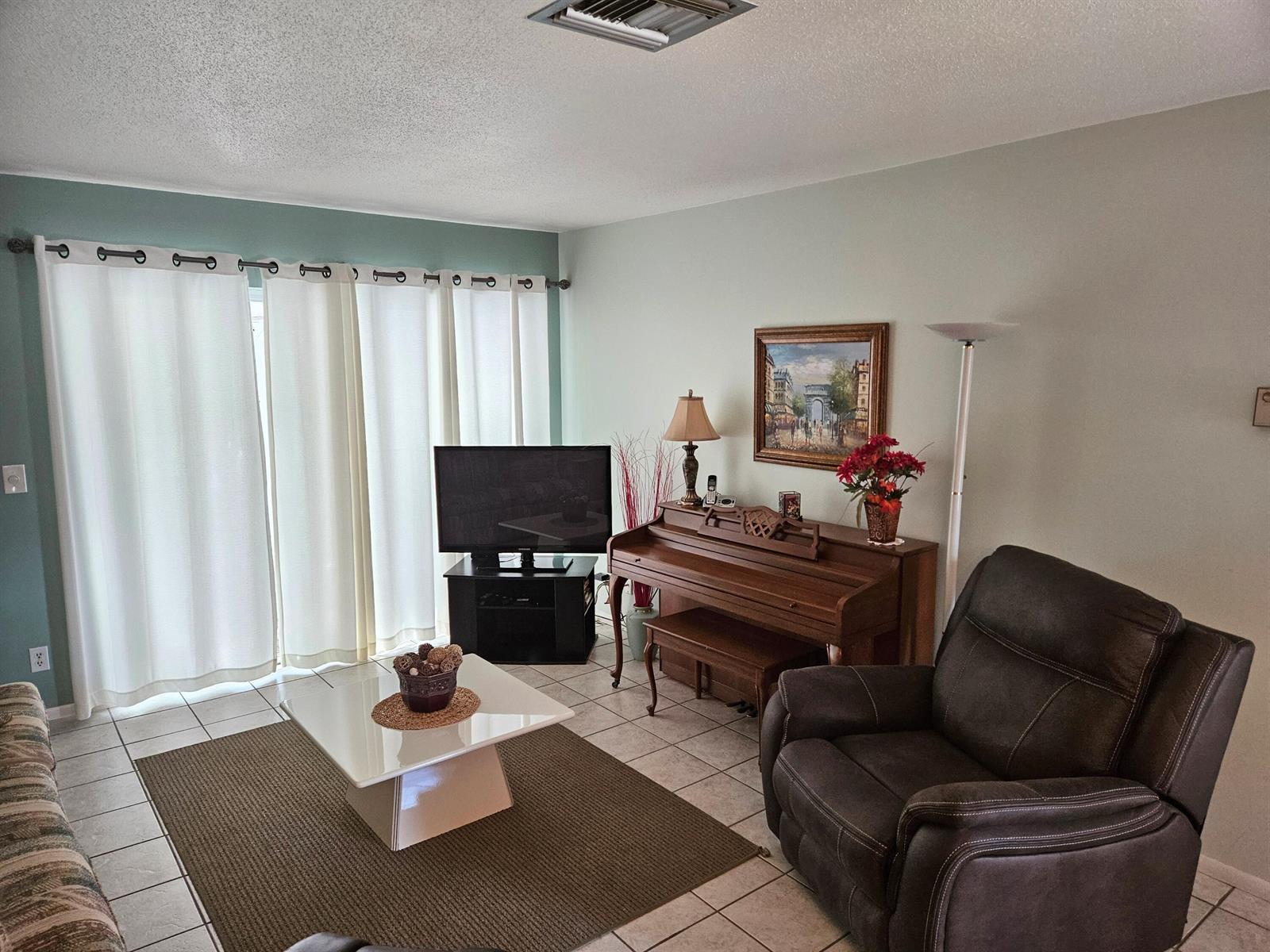 A living room features tile floors, a piano, a television, and a brown recliner — 2950 Crosley Drive E # D, West Palm Beach FL 33415, WEST PALM BEACH, FL