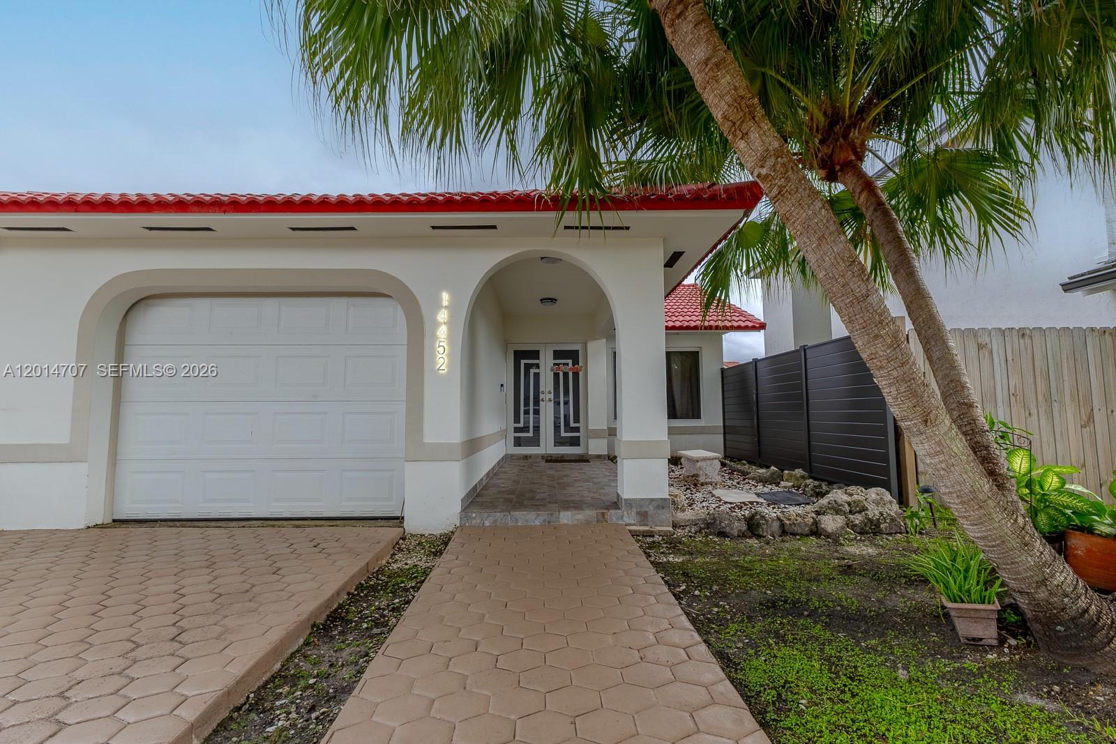 The exterior of a house features a white garage, arched entryway, and a palm tree — 14452 SW 115th St, Miami FL 33186, MIAMI, FL