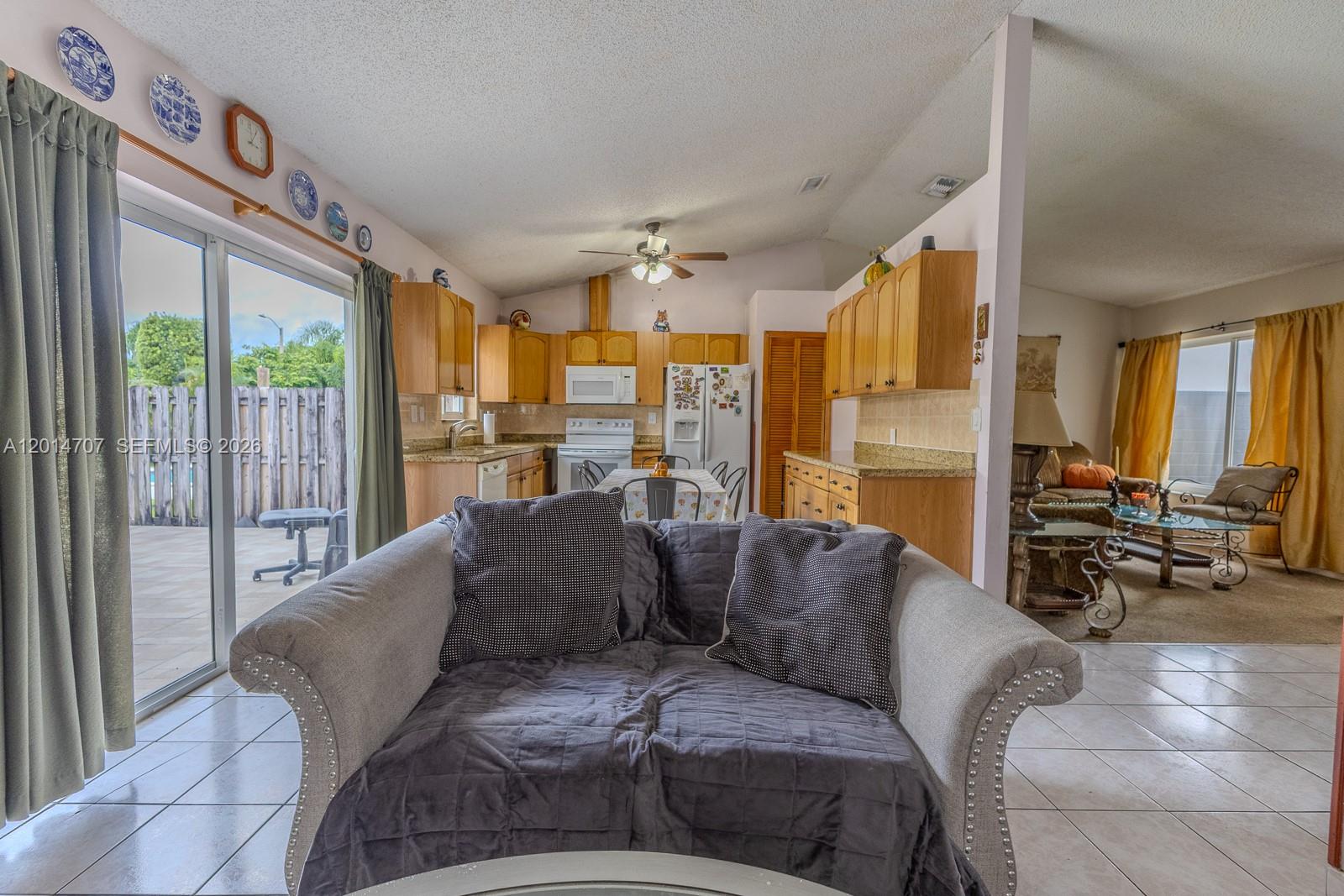 A living room with a gray loveseat overlooks an open-concept kitchen and a dining area — 14452 SW 115th St, Miami FL 33186, MIAMI, FL