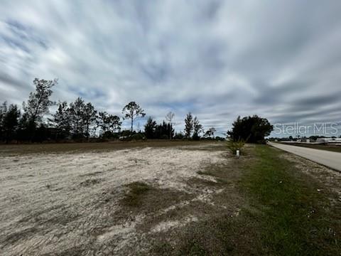 A wide, vacant, sandy lot sits beside a paved road under a cloudy sky — 1826 NE 37TH STREET, CAPE CORAL, FL