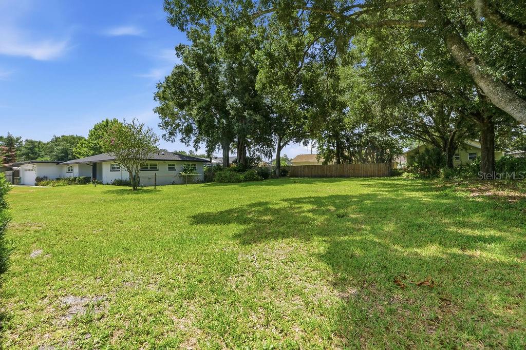 A large, grassy backyard features mature trees and a wooden fence behind a residential house — MILLINOCKETT LANE, ORLANDO, FL