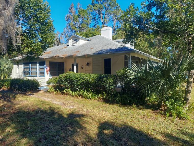 A light-colored, single-story house with a gray roof sits among trees and landscaping — 251 N BLUE LAKE AVENUE, DELAND, FL
