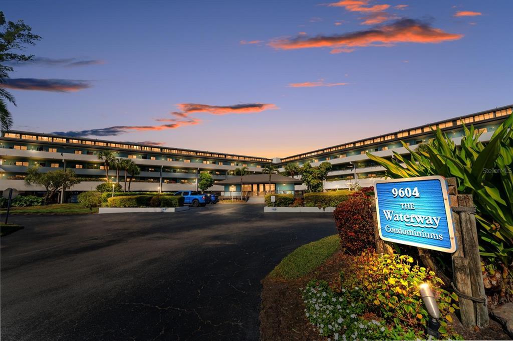 An exterior view of a multi-story condominium building at dusk with a prominent entrance sign — 9604 CORTEZ ROAD W UNIT 136, BRADENTON, FL