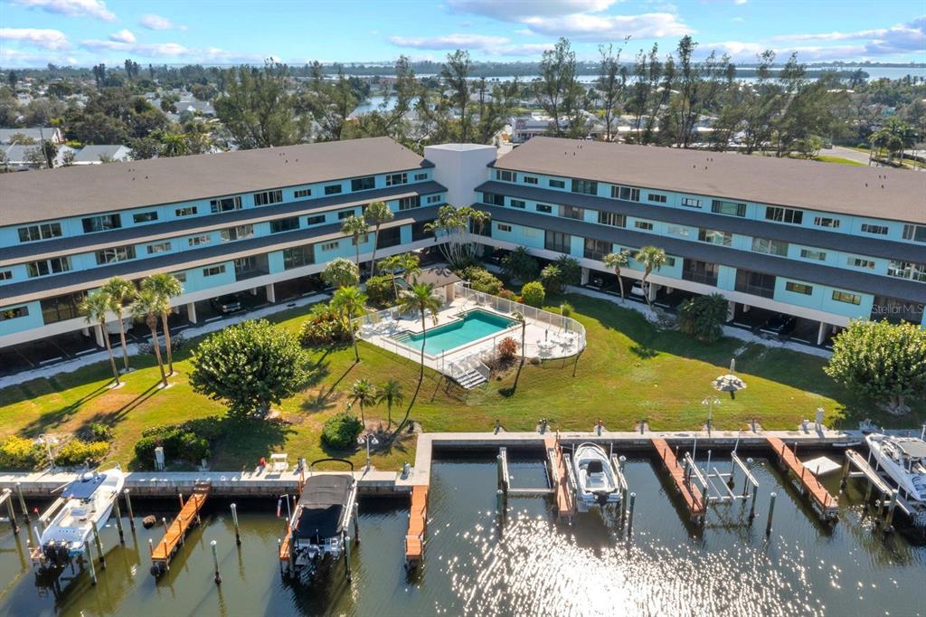 An aerial view shows a multi-story apartment building with a central pool and boat docks — 9604 CORTEZ ROAD W UNIT 136, BRADENTON, FL