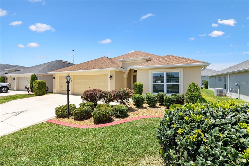 A single-story suburban house with a tan stucco exterior, shingled roof, and landscaped front yard — 4348 TUSCALOOSA PATH, THE VILLAGES, FL