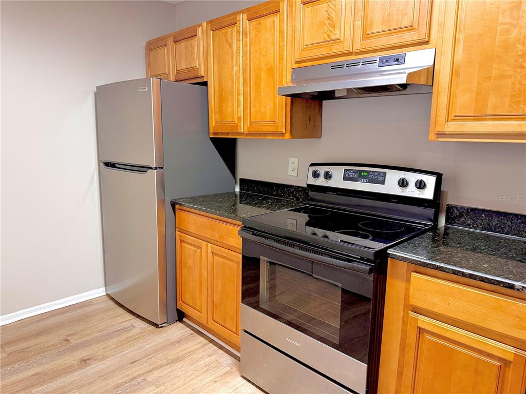 A kitchen features wooden cabinets, stainless steel appliances, and dark granite countertops — 644 KENWICK CIRCLE UNIT 104, CASSELBERRY, FL