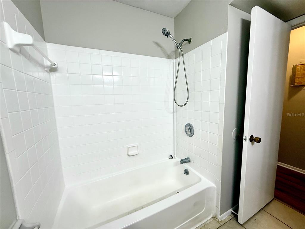 A white tiled bathtub and shower combination with a handheld showerhead in a bathroom — 644 KENWICK CIRCLE UNIT 104, CASSELBERRY, FL