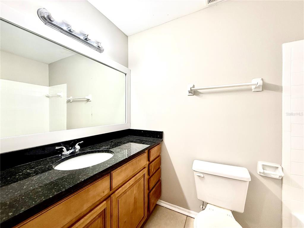 A bathroom features a wooden vanity with a black countertop, a mirror, and a toilet — 644 KENWICK CIRCLE UNIT 104, CASSELBERRY, FL