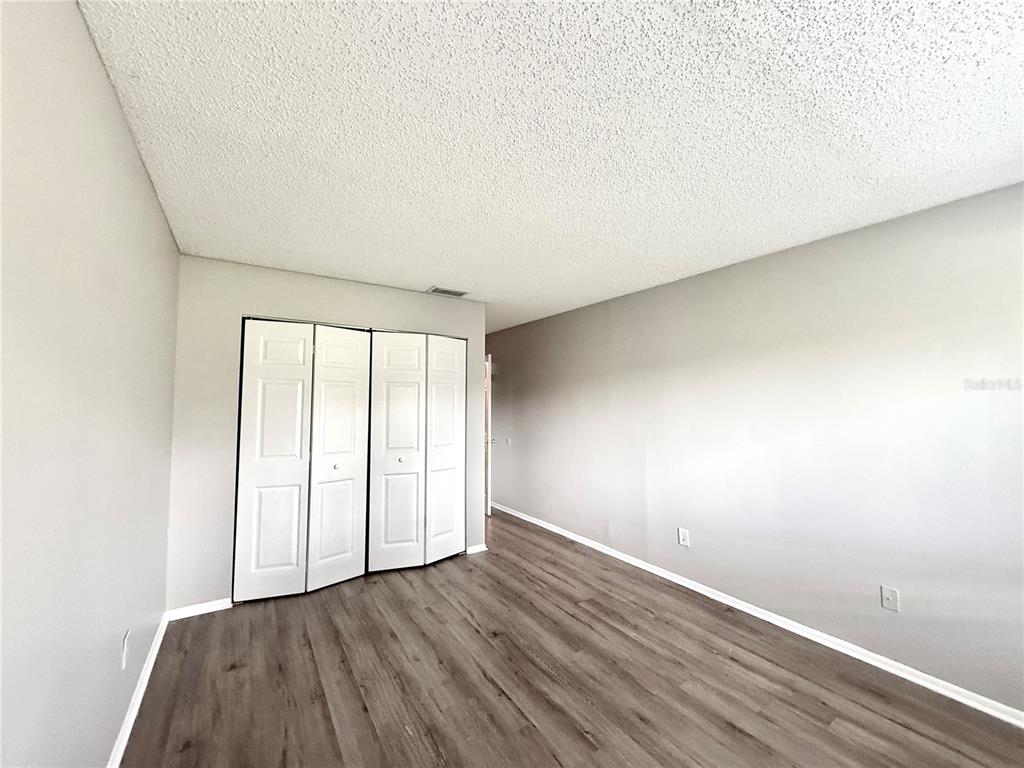 An empty bedroom features light gray walls, wood-look flooring, and white bifold closet doors — 644 KENWICK CIRCLE UNIT 104, CASSELBERRY, FL