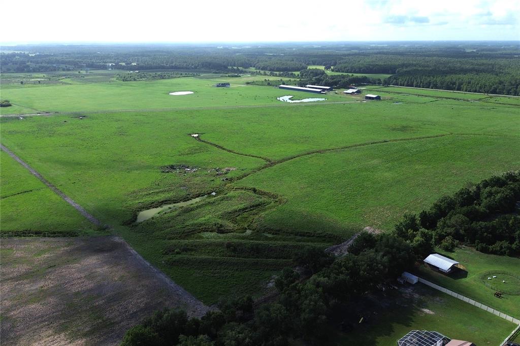 An aerial view shows a large, green pasture with a small pond and farm buildings — 14718 EVANS RANCH RD, LAKELAND, FL