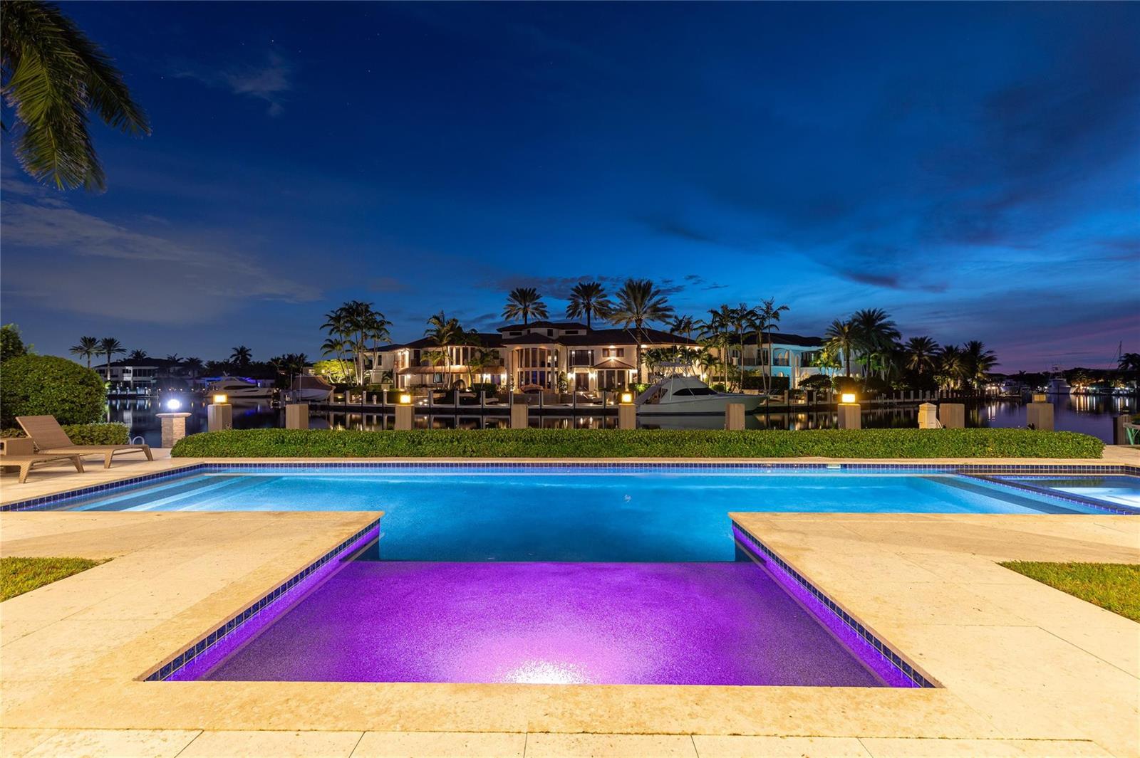 A swimming pool with a purple-lit spa overlooks a canal and a large waterfront mansion — 3211 NE 27th Avenue, Lighthouse Point FL 33064, LIGHTHOUSE POINT, FL
