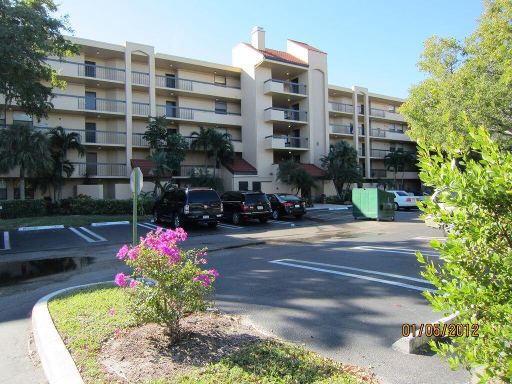 A multi-story apartment building with balconies stands behind a parking lot with several vehicles — 750 Egret Circle # 6103, Delray Beach FL 33444, DELRAY BEACH, FL