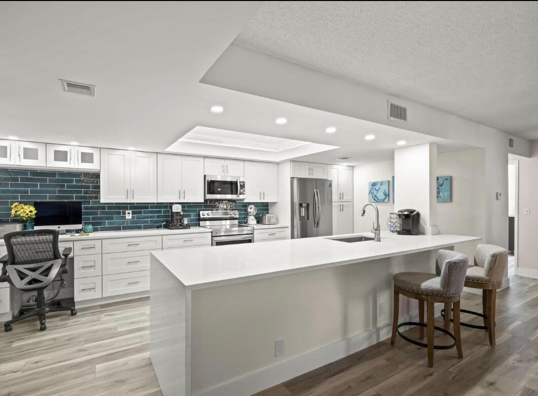 A modern kitchen features white cabinets, a large quartz island, and a blue tiled backsplash — 750 Egret Circle # 6103, Delray Beach FL 33444, DELRAY BEACH, FL