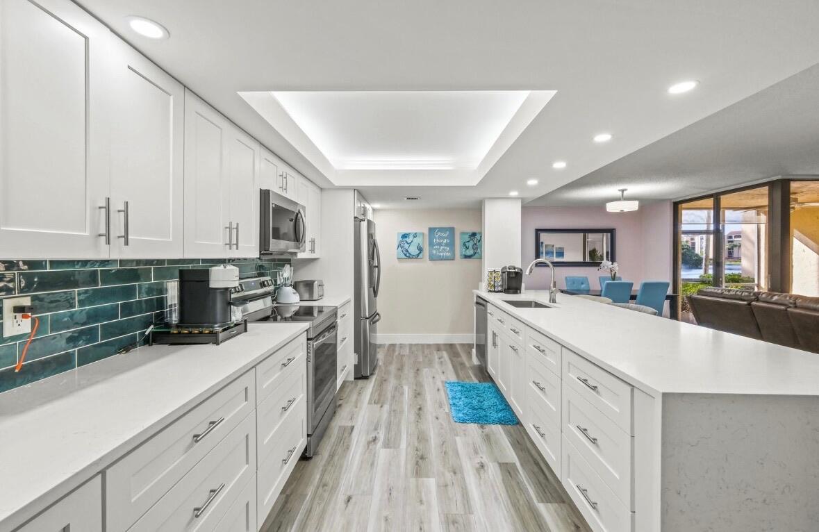 A modern kitchen features white cabinetry, a long quartz island, and teal subway tile backsplash — 750 Egret Circle # 6103, Delray Beach FL 33444, DELRAY BEACH, FL