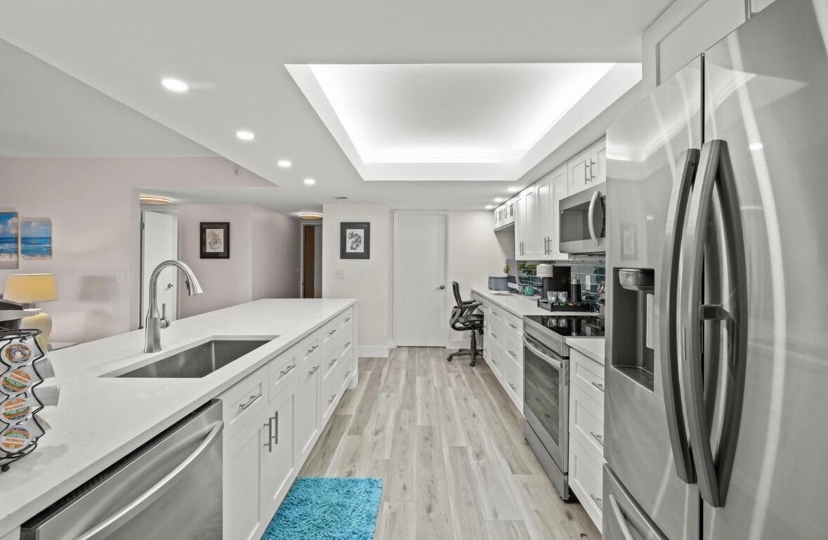 A modern white kitchen features a large island, stainless steel appliances, and recessed tray lighting — 750 Egret Circle # 6103, Delray Beach FL 33444, DELRAY BEACH, FL