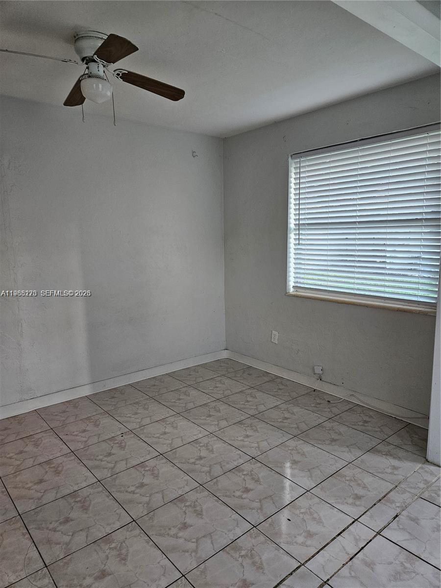 An empty room features light-colored tile flooring, white walls, a ceiling fan, and a window — 1437 NE 110th Ter # 4, Miami FL 33161, MIAMI, FL