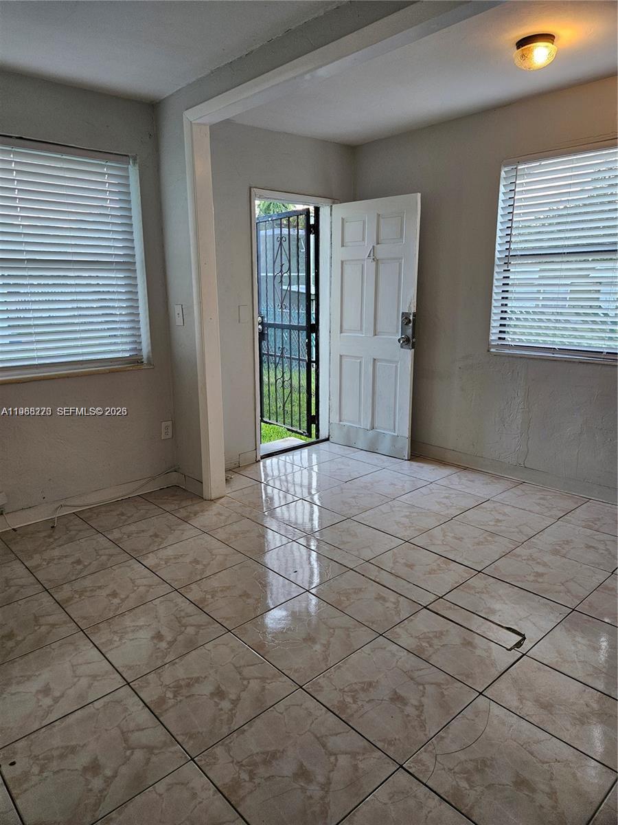 A room with light-colored tile flooring, two windows with blinds, and an open exterior door — 1437 NE 110th Ter # 4, Miami FL 33161, MIAMI, FL