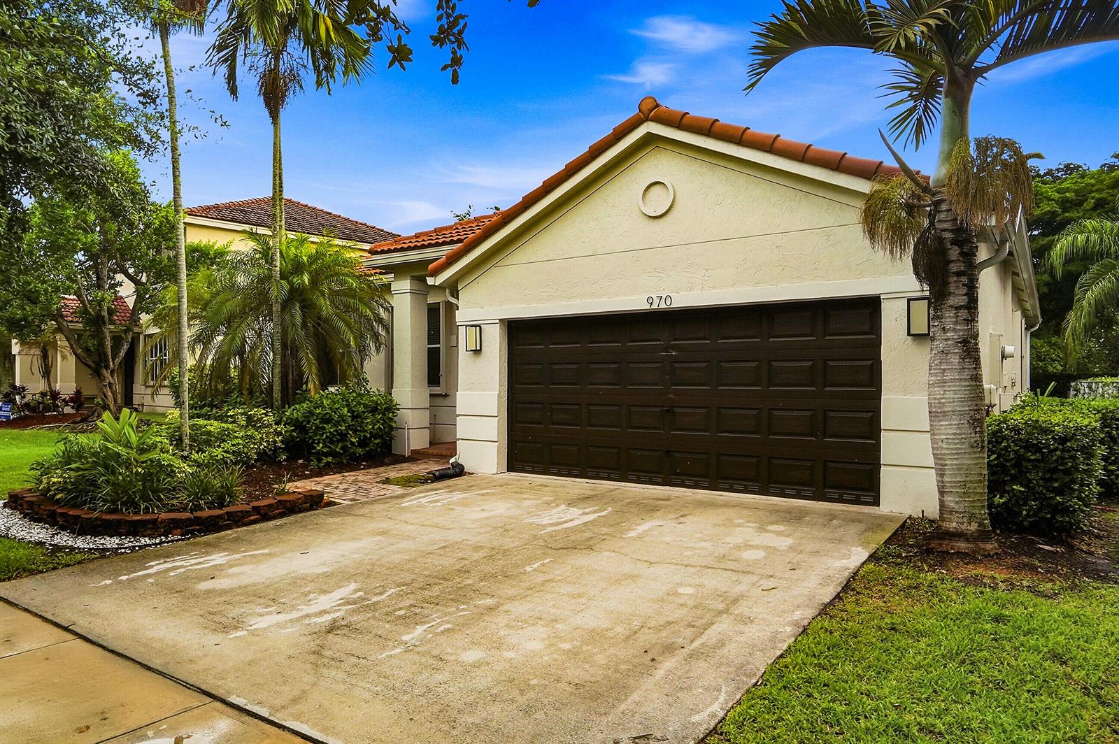 A tan house with a brown garage door, tile roof, and palm trees in the yard — 970 Tulip Circle, Weston FL 33327, WESTON, FL