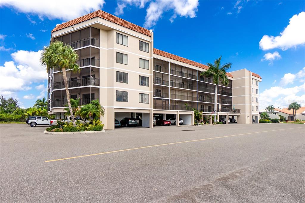A multi-story apartment building with a tiled roof, screened balconies, and ground-level covered parking — 25188 MARION AVENUE UNIT F207, PUNTA GORDA, FL