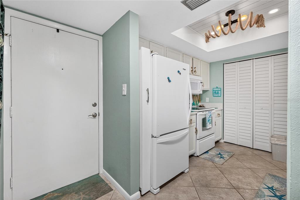 A kitchen features white appliances, light-colored cabinetry, tile flooring, and a decorative ceiling light fixture — 25188 MARION AVENUE UNIT F207, PUNTA GORDA, FL