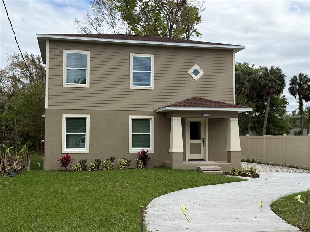 A two-story house with tan siding and stucco, a front porch, and a concrete driveway — 1119 WILLOW AVENUE, SANFORD, FL
