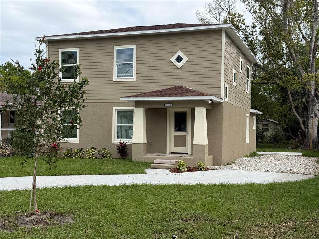 A two-story house with tan siding and stucco, featuring a covered porch and concrete driveway — 1119 WILLOW AVENUE, SANFORD, FL